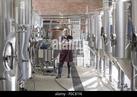 Ritratto di fabbricante di birra birreria, in piedi accanto a serbatoi in acciaio inox Foto Stock