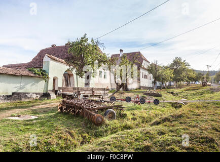 Macchine agricole al di fuori del tradizionale cottage rustico nella strada principale del villaggio sassone di Viscri, Romania Foto Stock