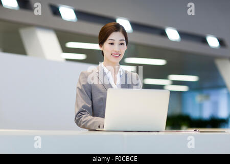 Fiducioso receptionist utilizzando computer portatile presso il banco di ricevimento Foto Stock