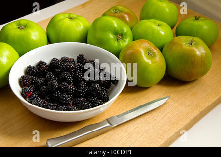 Bramley's mele con more in bianco ciotola con il coltello sul tagliere di legno Foto Stock