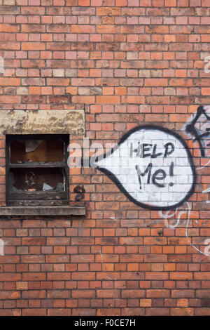 'Help Me!" parole di graffiti nel discorso bolla accanto a proveniente dalla rotta fracassato intavolato finestra sul rosso mattone parete auto sfondo Foto Stock