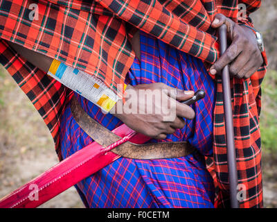 Le mani di un guerriero Massai tenendo un coltello tradizionale fissato ad una cinghia. Orologio moderno dall'altra. Foto Stock