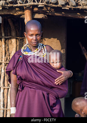 Maasai madre con il suo bambino di fronte a una casa tradizionale nel loro boma (paese) di Tan Foto Stock