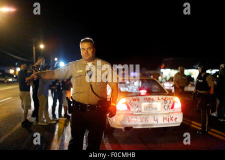 Ferguson, STATI UNITI D'AMERICA. 11 Ago, 2015. Un poliziotto si allontana un gruppo di dimostranti durante una manifestazione in Ferguson, gli Stati Uniti, il 11 agosto, 2015. Le proteste dell'anniversario della ripresa di disarmato 18-anno-vecchio Michael Brown sono state estese per una seconda giornata di martedì in Ferguson. Lo stato di emergenza è stato dichiarato per la città di Ferguson il lunedì a seguito di scontri tra polizia e manifestanti domenica notte. © Jim Vondruska/Xinhua/Alamy Live News Foto Stock