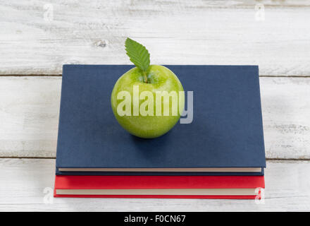 Una sana mela verde sulla parte superiore di libri con rustico in legno bianco in background. Il concetto di istruzione di ritorno a scuola. Foto Stock
