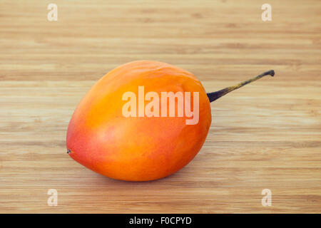 Close-up di un intero tamarillo (anche noto come albero di pomodoro (Solanum betaceum)) su un tagliere di legno. Foto Stock