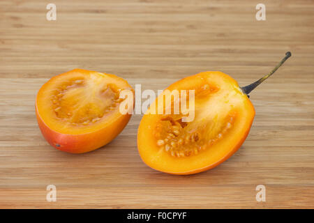 Close-up di un tamarillo (anche noto come albero di pomodoro (Solanum betaceum) tagliato a metà su un tagliere di legno. Foto Stock