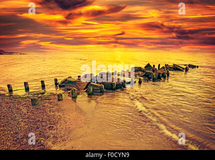 Vintage tonica drammatico tramonto sulla spiaggia e molo roccioso. Foto Stock