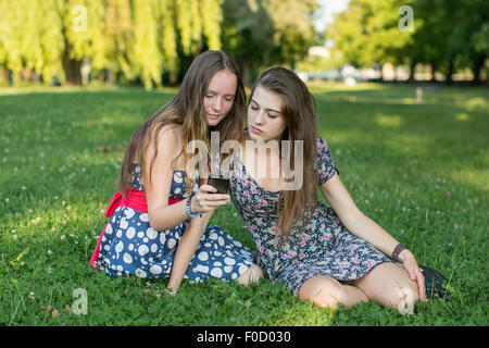 Due giovani ragazze seduto sull'erba e utilizzare uno smartphone. Foto Stock