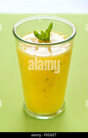 Il raffreddamento di Mango frullato di menta, bevanda estiva sul tavolo verde, giallo frullato tropicale fatta con mango, menta e il succo di lime. Foto Stock
