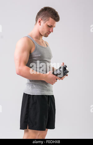 Attraente giovane azienda protein shake bottiglia. Contro lo sfondo grigio, sorridente e lo sta guardando Foto Stock