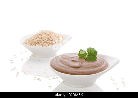 Tahini e pasta di semi di sesamo nella ciotola bianco isolato su sfondo bianco. Hummus ingredienti, la dieta mediterranea. Foto Stock