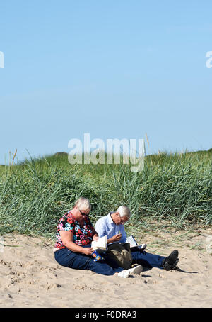 Anziana coppia seduta completamente vestito sulla spiaggia sabbiosa di Fleetwood, nel Lancashire, Regno Unito Foto Stock