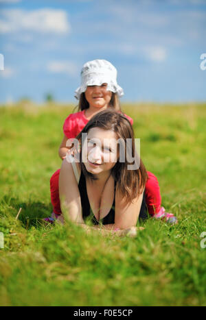 Mamma e figlia piccola nel prato in erba verde. Soleggiata giornata estiva. Profondità di campo. Messa a fuoco selettiva su madre Foto Stock