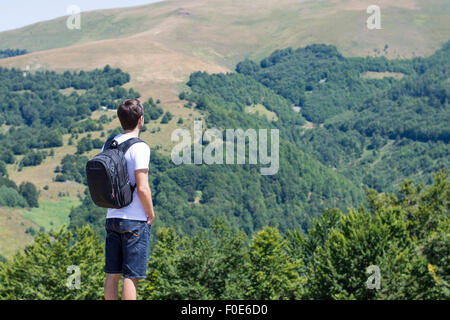 Giovane uomo con zaino in piedi su cliff's edge e cercando di montagna. Avventura Trekking Foto Stock