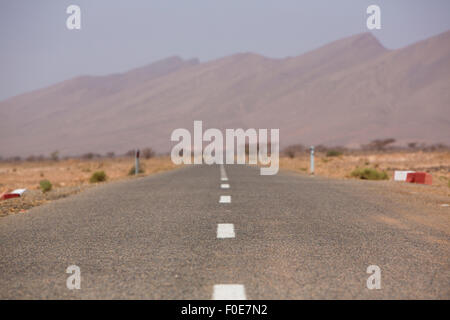 Strada diritta attraverso il deserto nella regione di Tata, montagne sullo sfondo. Il Marocco, Africa Foto Stock