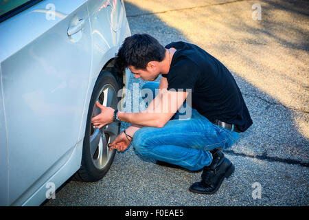 Bel giovane in abbigliamento Casual Squatting oltre al volante di una sua vettura bianca cambio pneumatici Foto Stock