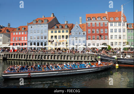 Canal tour in barca girando intorno nelle affollate Nyhavn su una calda e soleggiata giornata estiva piena di turisti e visitatori anche sul pontile. Visite canal cruise. Foto Stock