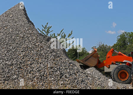 Escavatore davanti a un cumulo di macerie al di fuori di una miniera contro il cielo blu Foto Stock