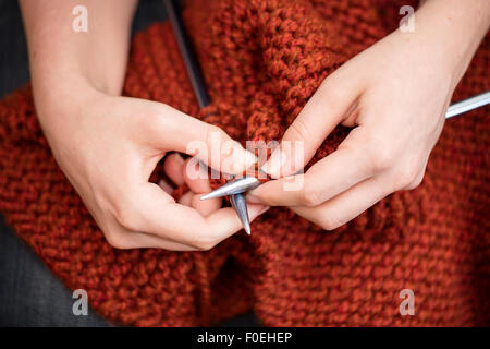 Giovane donna maglia una sciarpa con filato marrone rossiccio. Foto Stock