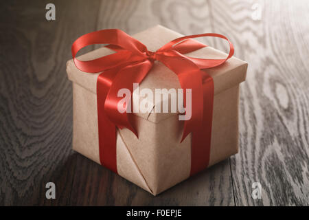 Rustico presente scatola con nastro rosso sul tavolo di legno Foto Stock