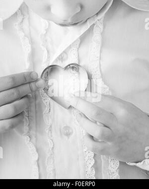 Bambina di contenimento a forma di cuore formina nelle sue mani. Immagine concettuale di infanzia, di amore e di affetto. Foto Stock