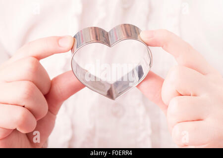 Bambina di contenimento a forma di cuore formina nelle sue mani. Immagine concettuale di infanzia, di amore e di affetto. Foto Stock