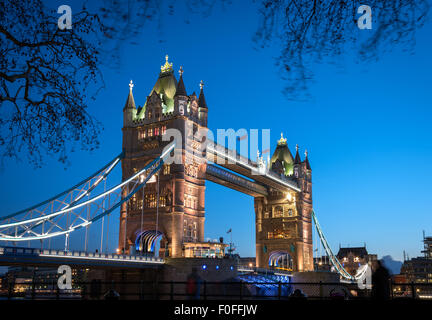 Vista del Tower Bridge di Londra dalle rive del Tamigi. Esso è il più visitato landmark. Bridge è illuminato in blu ora. Foto Stock
