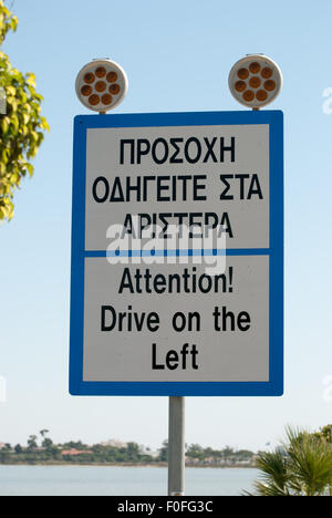 Cartello stradale "Attenzione! Guidare a sinistra!' con il lago di sale come uno sfondo closeup. Larnaca. Cipro. Foto Stock