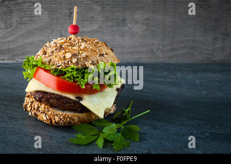 Hamburger Gourmet con il formaggio svizzero, verdure fresche su multigrain bun contro lo sfondo scuro e spazio di copia Foto Stock