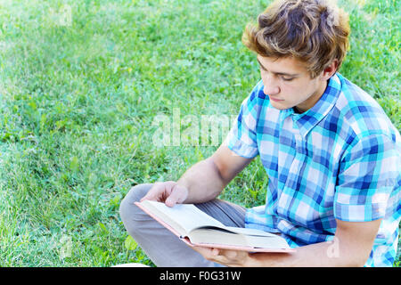 Giovane uomo è seduto e la lettura di un libro sull'erba Foto Stock