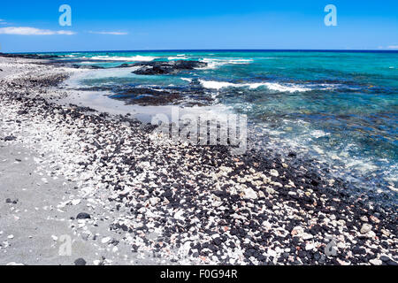 Un bel bianco e nero spiaggia di ghiaia con chiare acque blu su una spiaggia remota in Kona Hawaii. Foto Stock