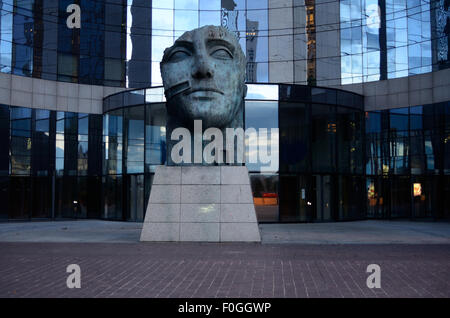 Una statua in bronzo del capo di un uomo circondato da un moderno, vetro edificio per uffici. Foto Stock