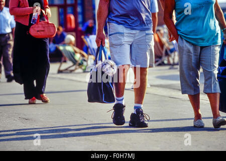 Un giovane che porta un piccolo cane in un sacchetto di shopping lungo la promenade. Blackpool. Lancashire. Regno Unito Foto Stock
