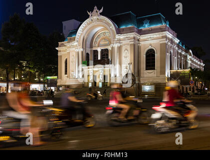 Vista notturna di motociclisti che passa in una sfocatura di fronte all'illuminato (Saigon Ho Chi Minh City) Opera House Foto Stock