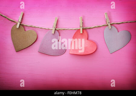 Realizzata a mano con cuori di carta appeso con clothespins su rosa tagliere in legno Foto Stock