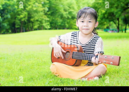 Asian bambini seduti su erba e giocare ukulele in posizione di parcheggio Foto Stock