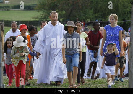 A Taizé, Francia. Il 16 agosto 2015. Frère Alois, priore della comunità di Taizé, lascia la preghiera, circondato da bambini. I fratelli di Taizé, insieme a migliaia di pellegrini e i leader della Chiesa da molti diversi denominazione, terrà una preghiera di ringraziamento a Dio in memoria di Frère Roger in occasione del decimo anniversario della sua morte e nell'anno del suo centesimo compleanno e il settantacinquesimo anniversario del suo arrivo a Taizé. Foto Stock