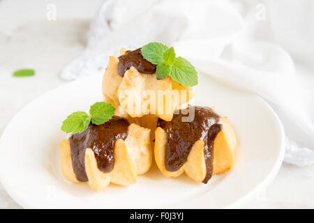 Profiteroles con crema e salsa al cioccolato e menta sulla piastra bianca Foto Stock