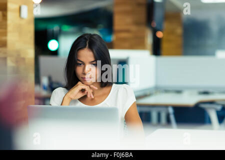 Ritratto di un grave imprenditrice utilizzando computer portatile in ufficio Foto Stock