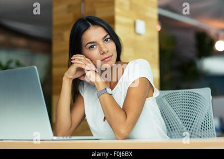 Ritratto di attraente pensieroso imprenditrice seduto alla scrivania in ufficio e guardando la fotocamera Foto Stock