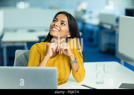 Ritratto di un felice imprenditrice seduto al suo posto di lavoro in ufficio e guardando in alto Foto Stock