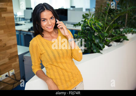 Ritratto di un felice bella imprenditrice parlando al telefono in ufficio Foto Stock