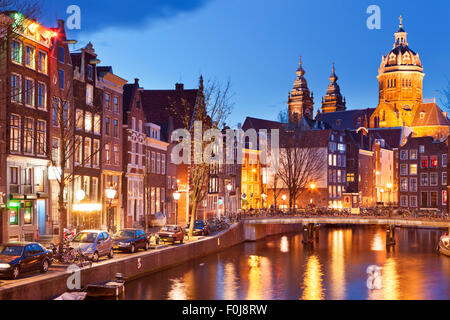 Un canale nel quartiere a luci rosse di Amsterdam, Paesi Bassi con la chiesa di San Nicola alla fine. Fotografato di notte. Foto Stock