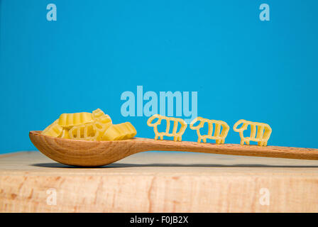 La pasta in forma di animali e un cucchiaio di legno su uno sfondo blu Foto Stock