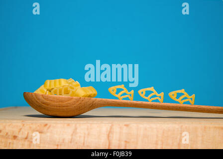 La pasta in forma di animali e un cucchiaio di legno su uno sfondo blu Foto Stock