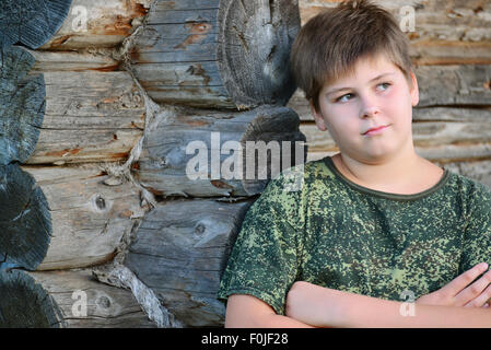 Teen Boy in camuffamento sorge vicino a parete in legno Foto Stock