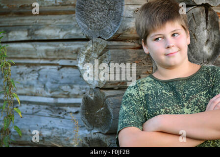 Teen Boy in camuffamento sorge vicino a parete in legno Foto Stock