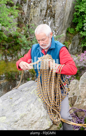 Maschio esperto rocciatore disimballaggio di una fune di arrampicata in cima ad una rupe salita. Il Galles del Nord, Regno Unito, Gran Bretagna Foto Stock