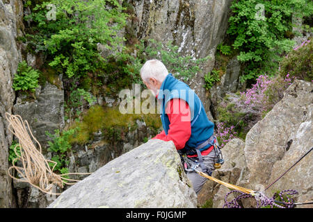 Sperimentato belayed rocciatore gettando una fune di arrampicata verso il basso dalla sommità di una rupe a salire. Snowdonia, il Galles del Nord, Regno Unito, Gran Bretagna Foto Stock